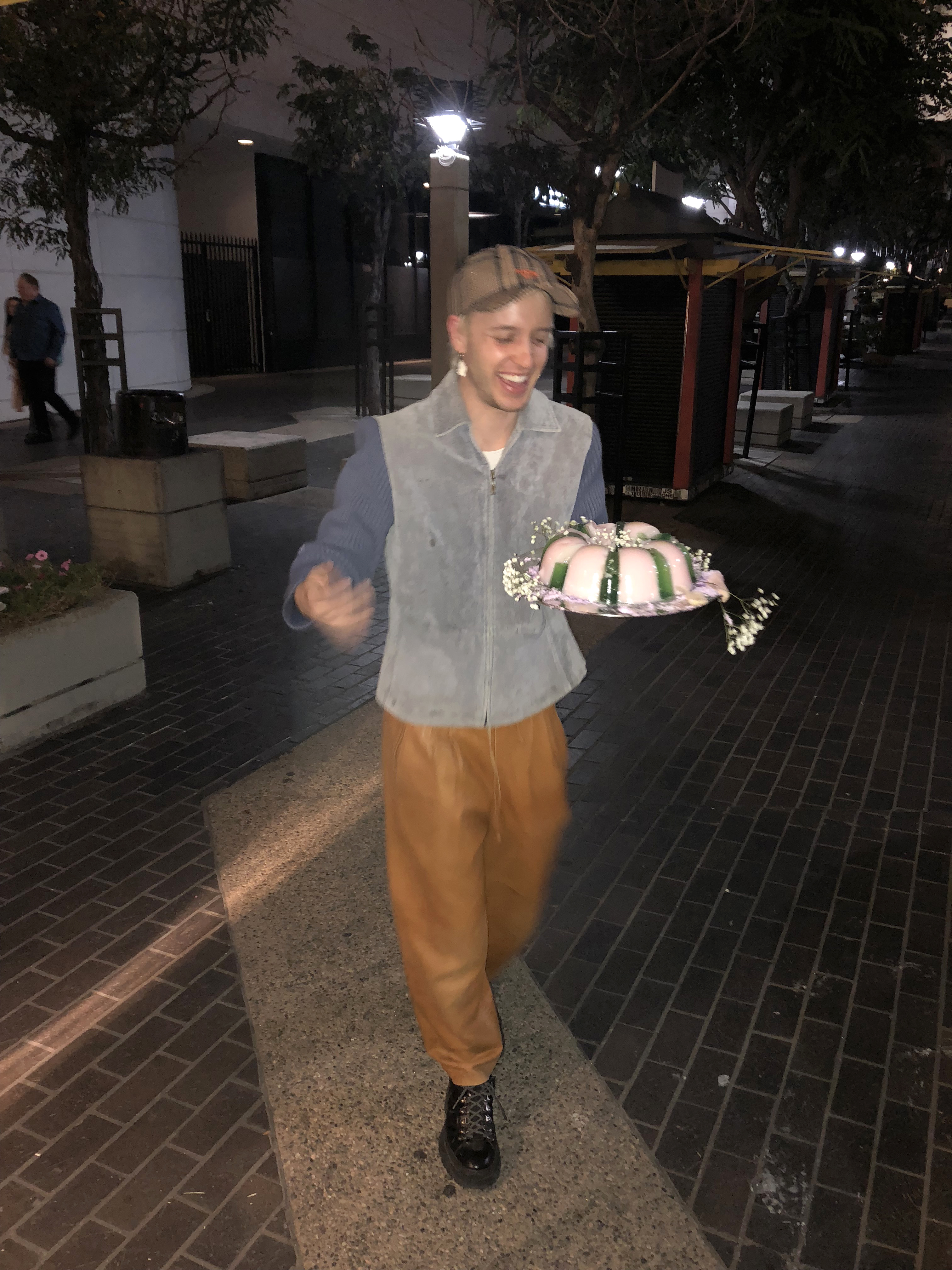 A man holding a jello cake and laughing while walking towards the camera